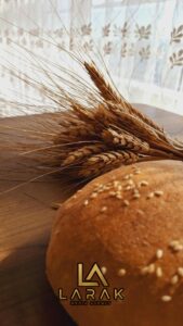 Close-up of a sesame seed bun with wheat sprigs on a wooden table, sunlit.